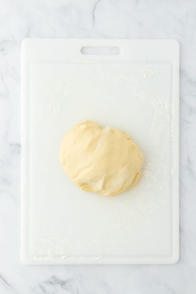 A ball of dough resting on a floured white cutting board