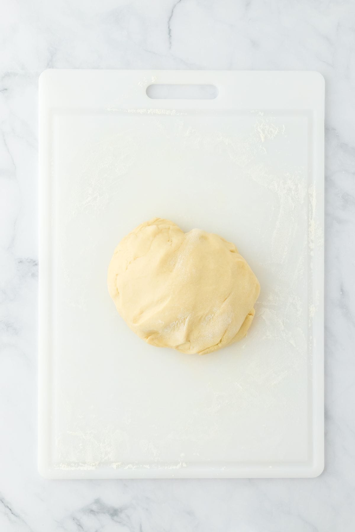 A ball of dough resting on a floured white cutting board