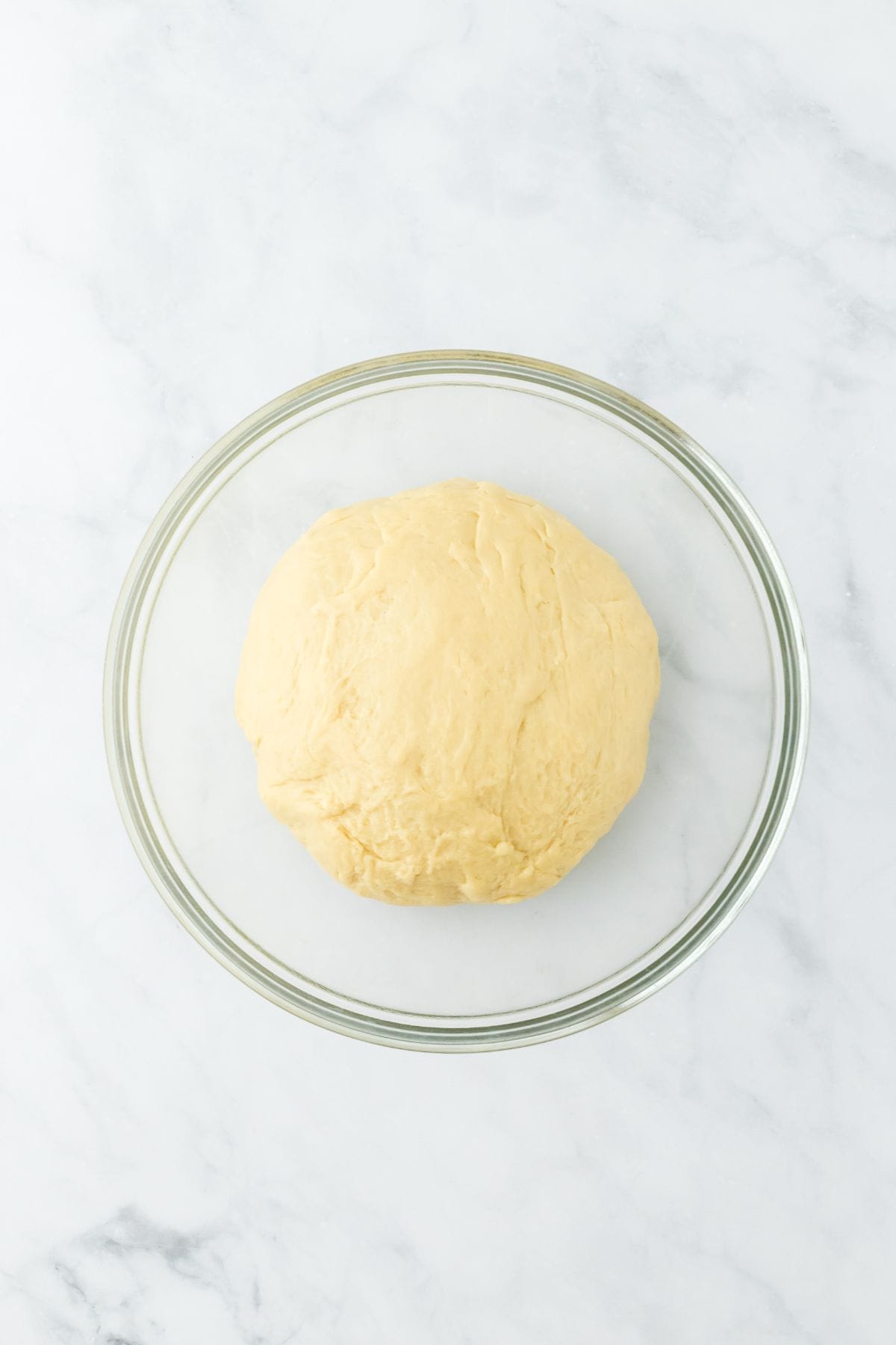 A round ball of dough placed in a clear glass bowl