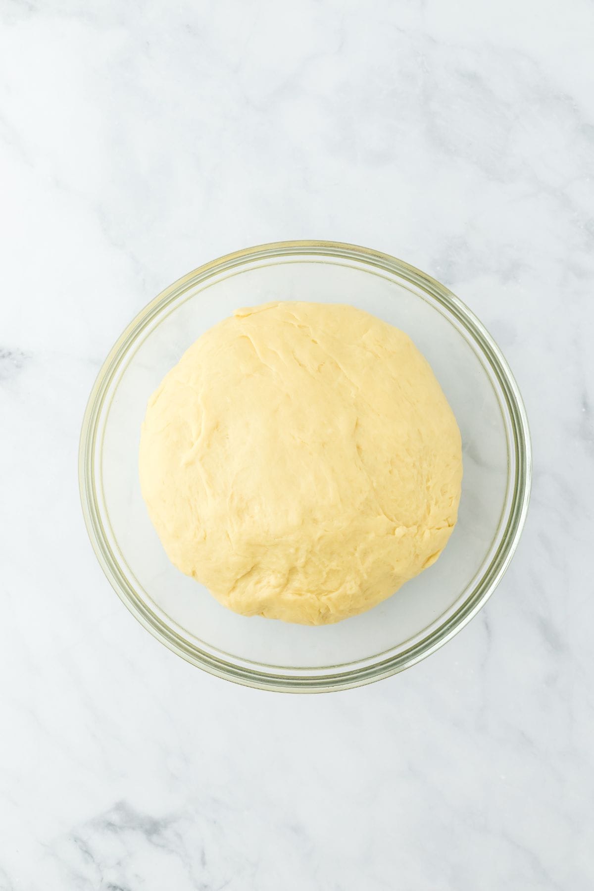 A ball of risen dough in a clear glass bowl