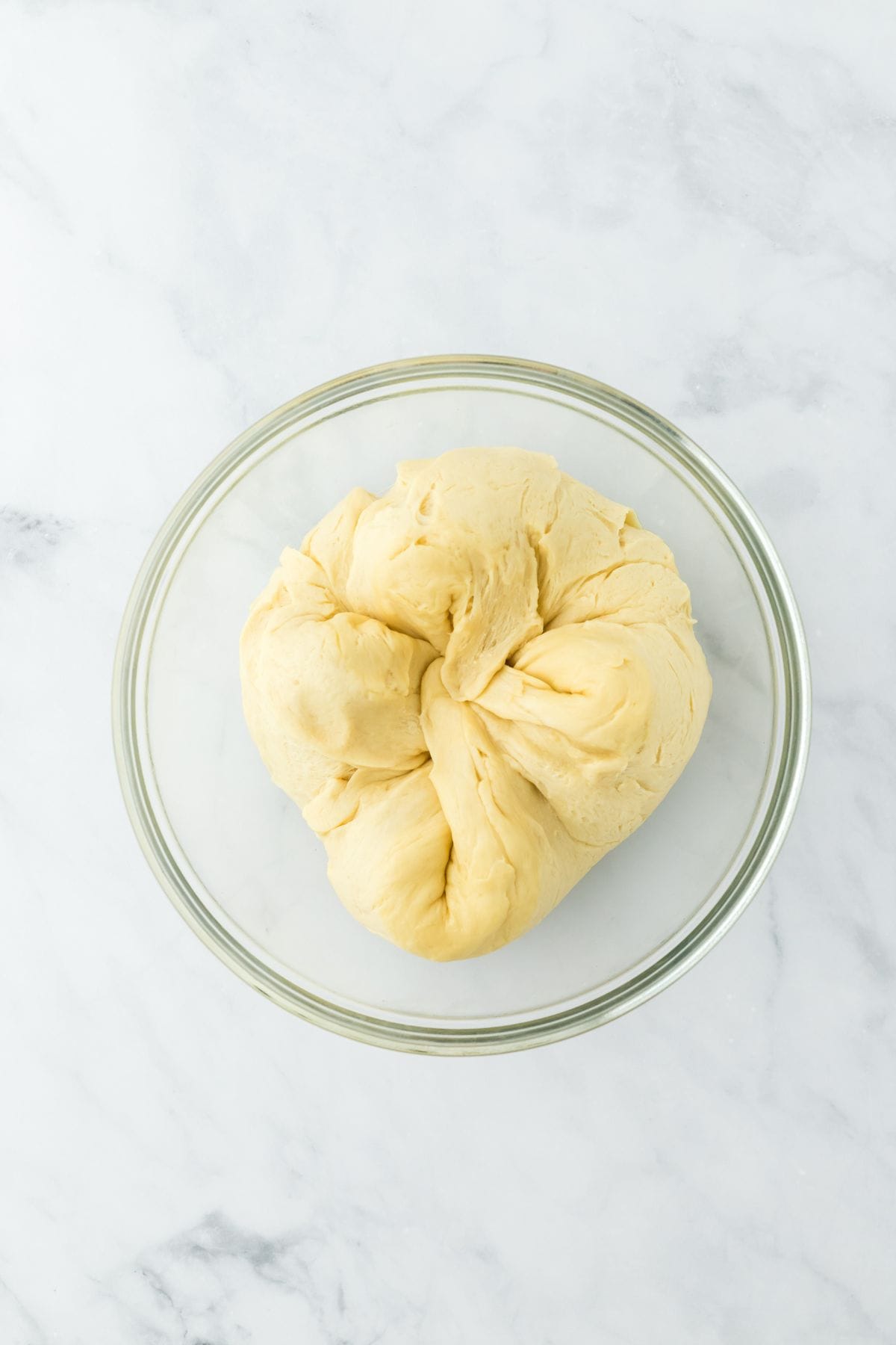 Deflated dough and twisted into a knot in a glass bowl