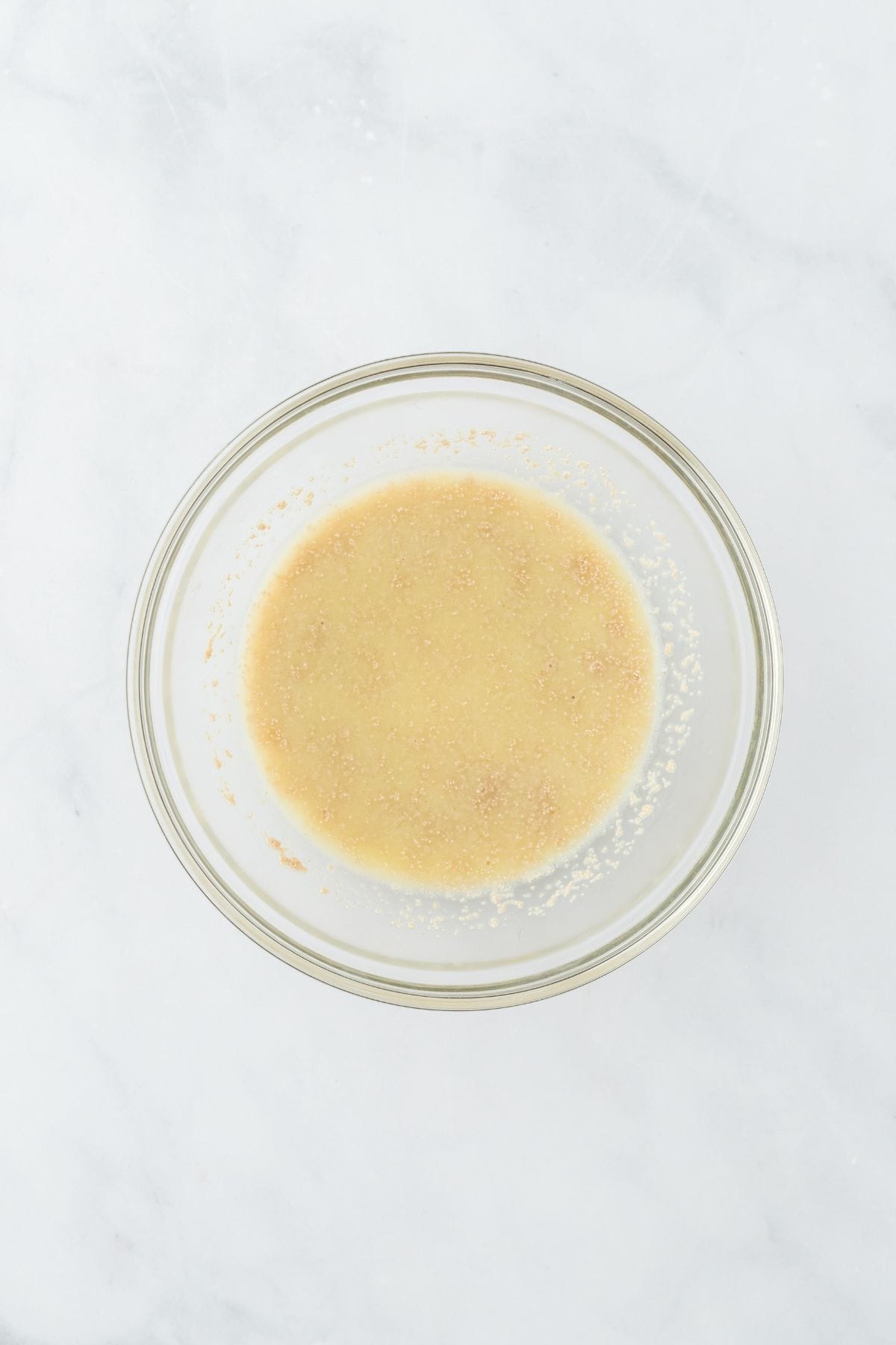 A glass bowl containing yeast that has been activated in warm water, forming bubbles on the surface