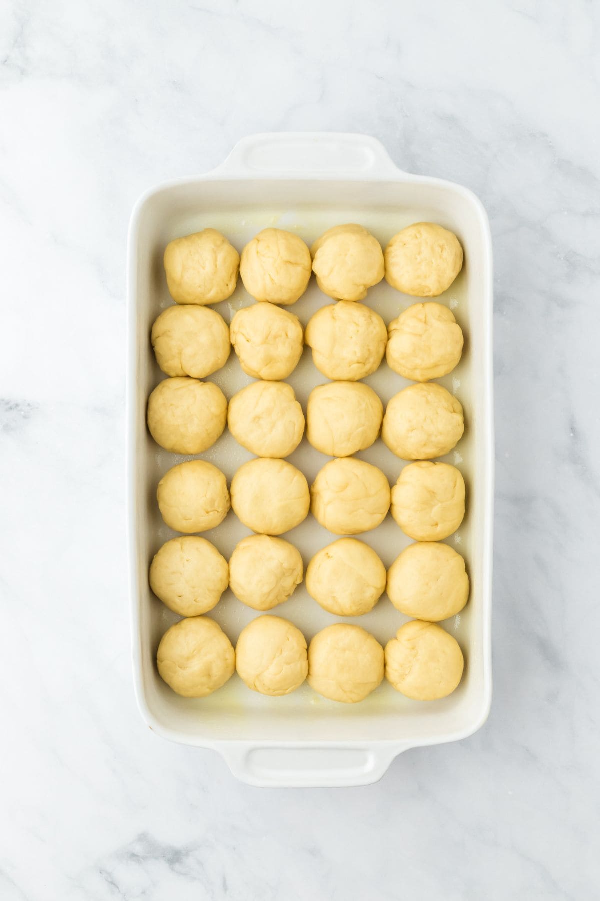 Small round dough pieces arranged neatly in a greased baking dish