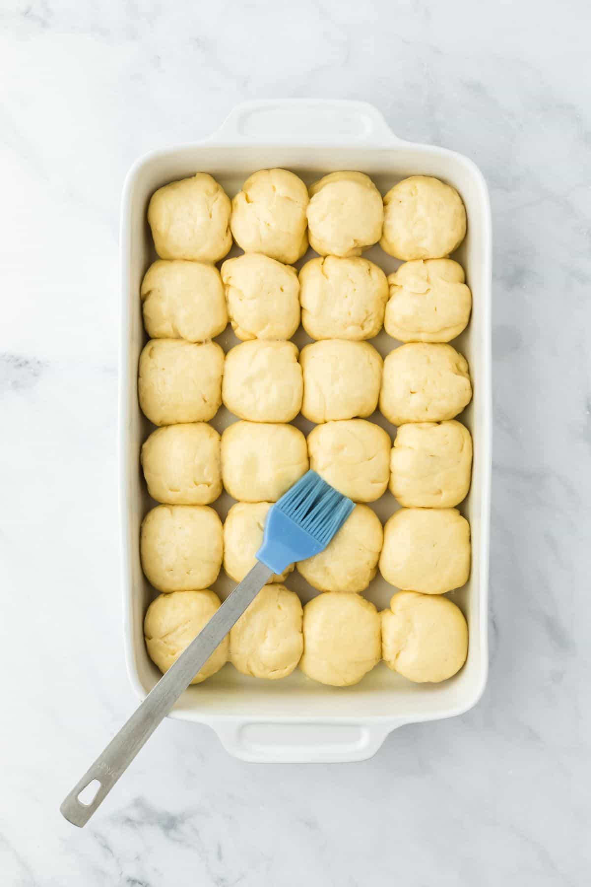 Dough pieces in the dish being brushed with melted butter before baking