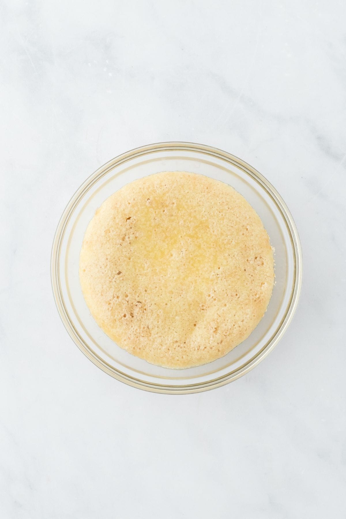 A glass bowl filled with risen yeast dough, smooth and puffed up after proofing