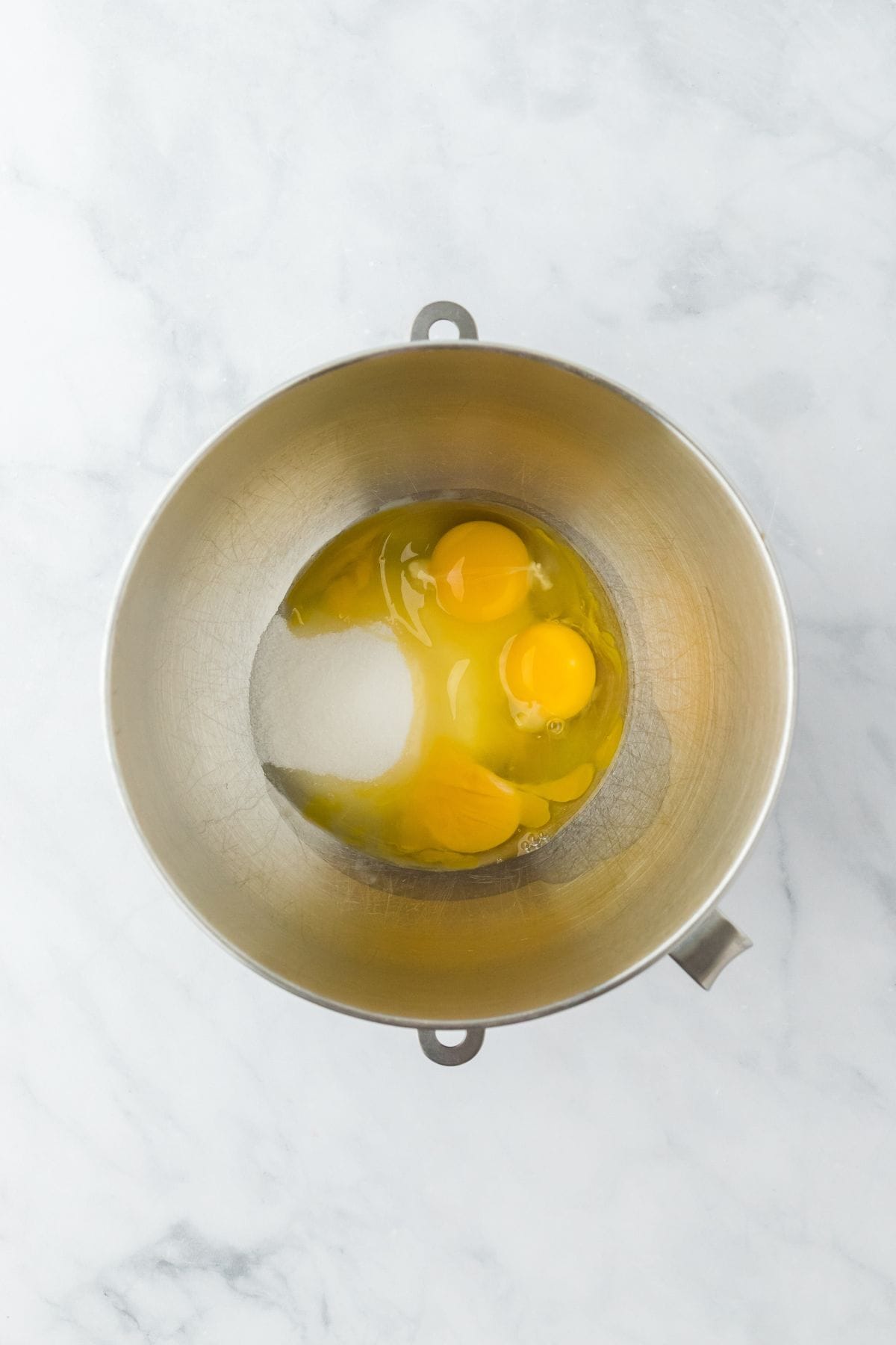 A bowl with eggs and sugar in a metal mixing bowl, ready for mixing