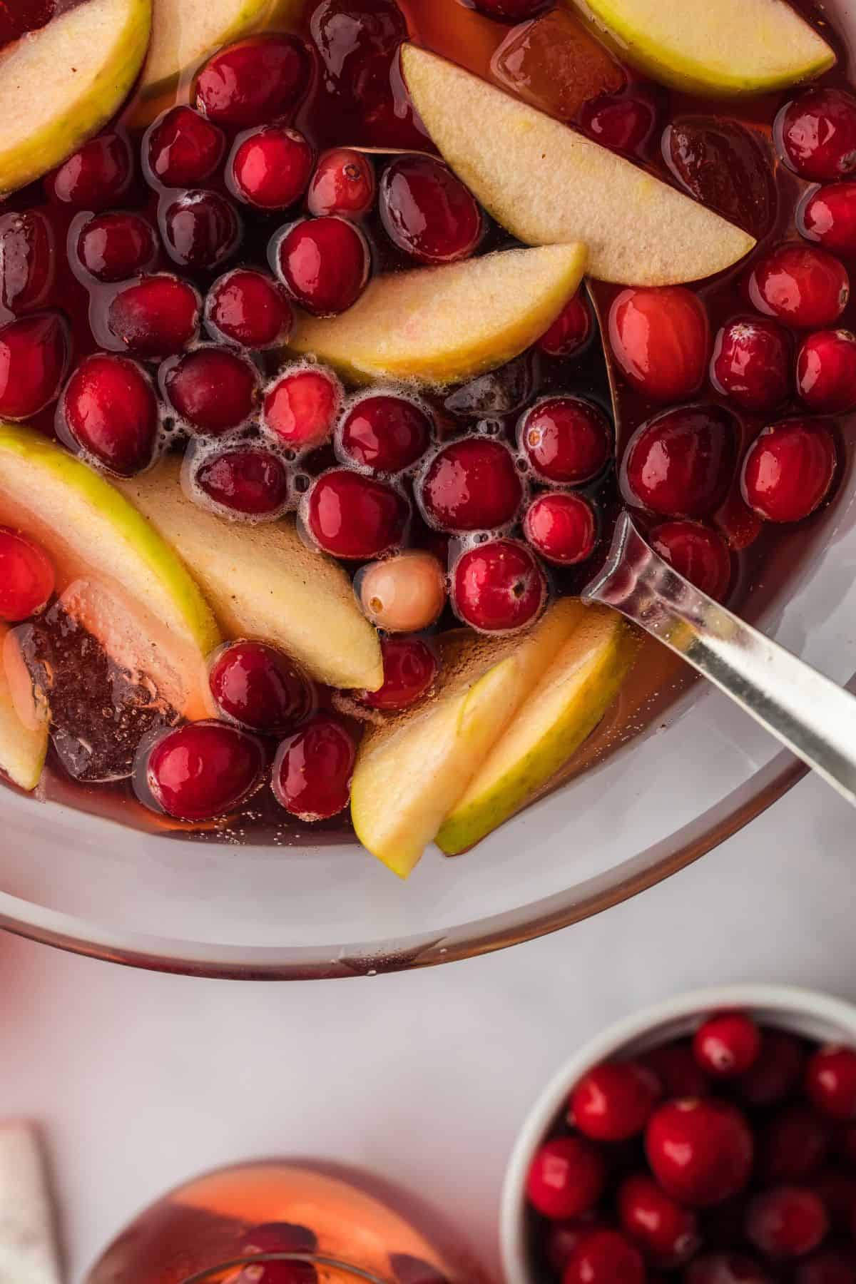 Closeup view of a punch bowl filled with red Thanksgiving punch, cranberries, apple slices, and a ladle