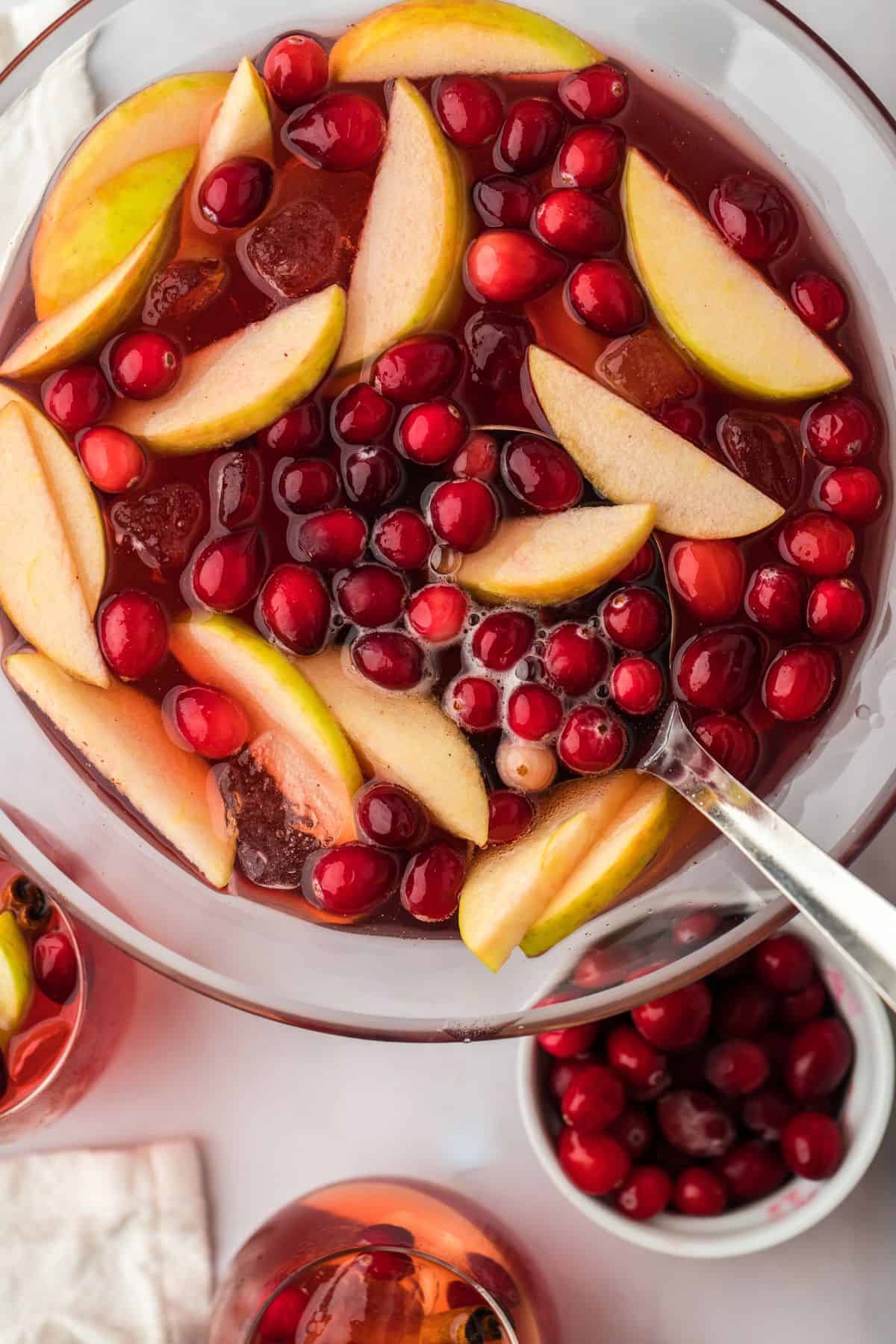 Overhead view of the Thanksgiving punch bowl filled with cranberries, apple slices, and a ladle, with a small bowl of cranberries nearby