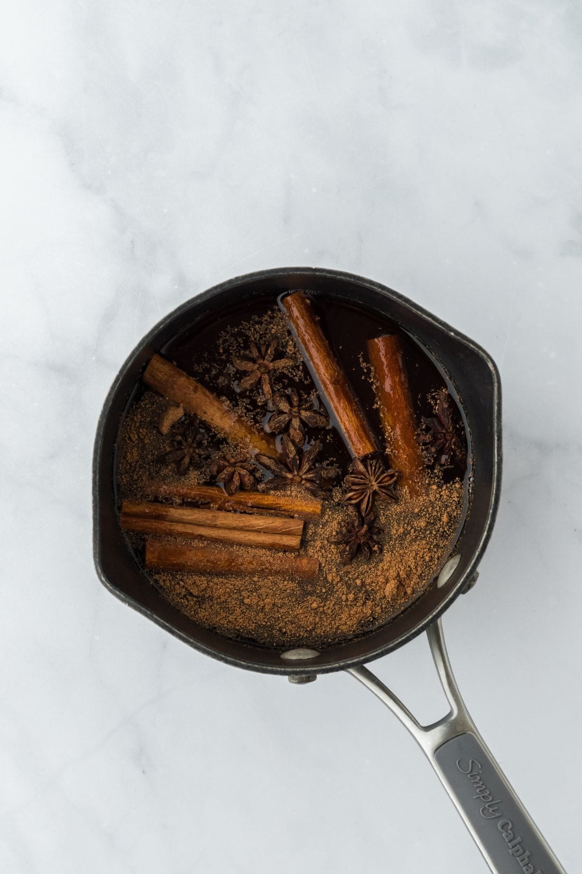 Overhead shot of a saucepan with cinnamon sticks, star anise, and spices simmering in liquid