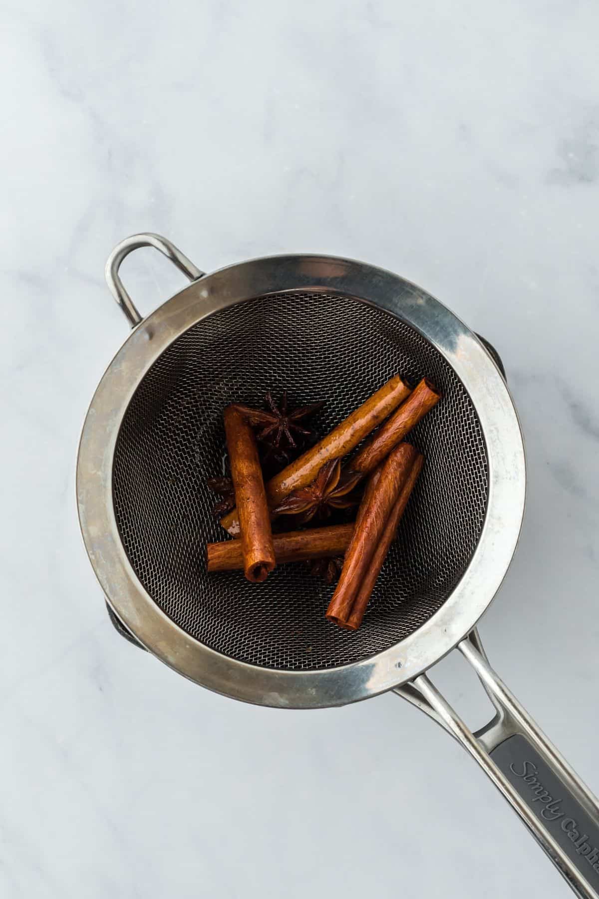 Overhead shot of a sieve straining out cinnamon sticks and star anise