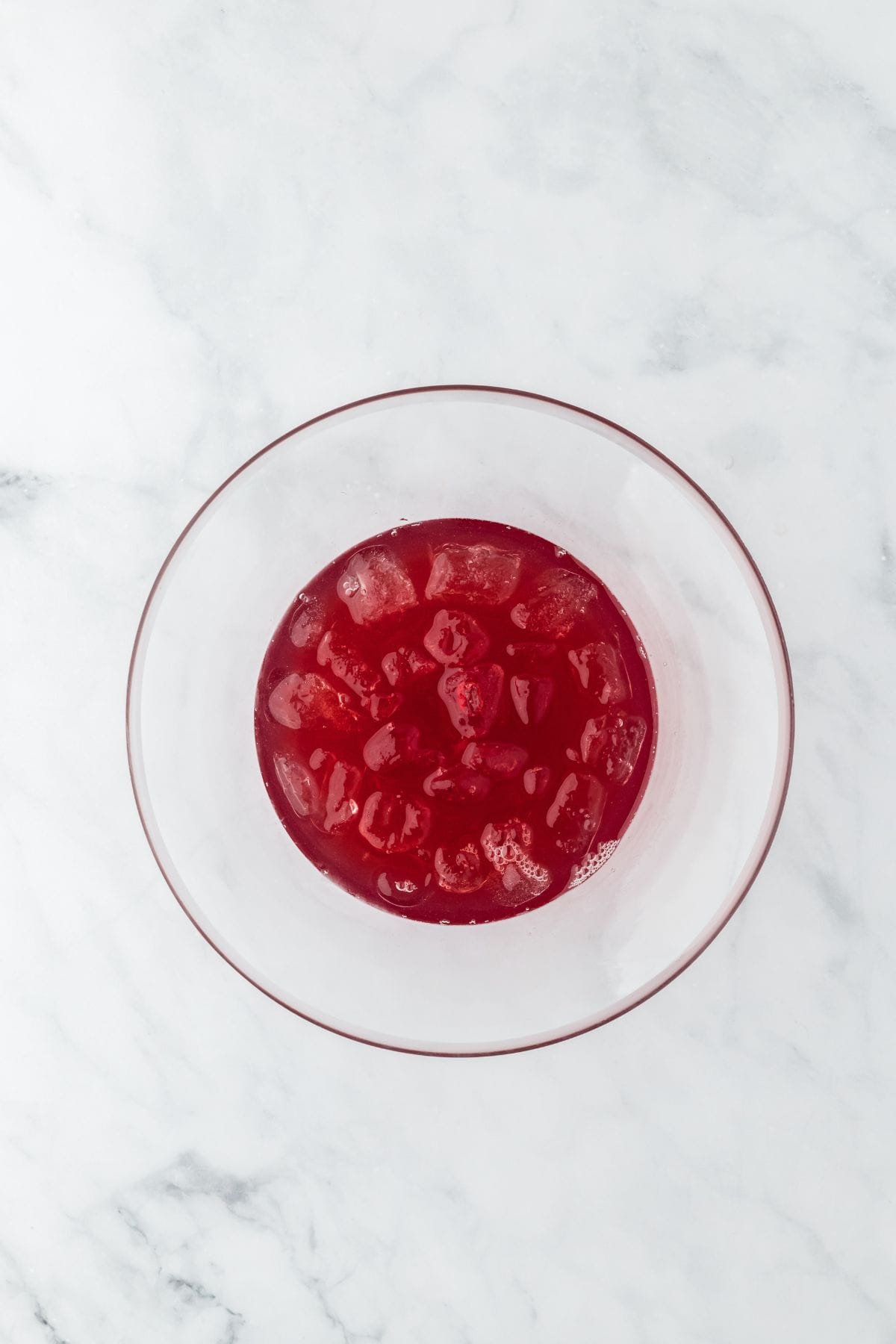 Overhead shot of a bowl filled with syrup, cranberry and lime juice and ice cubes