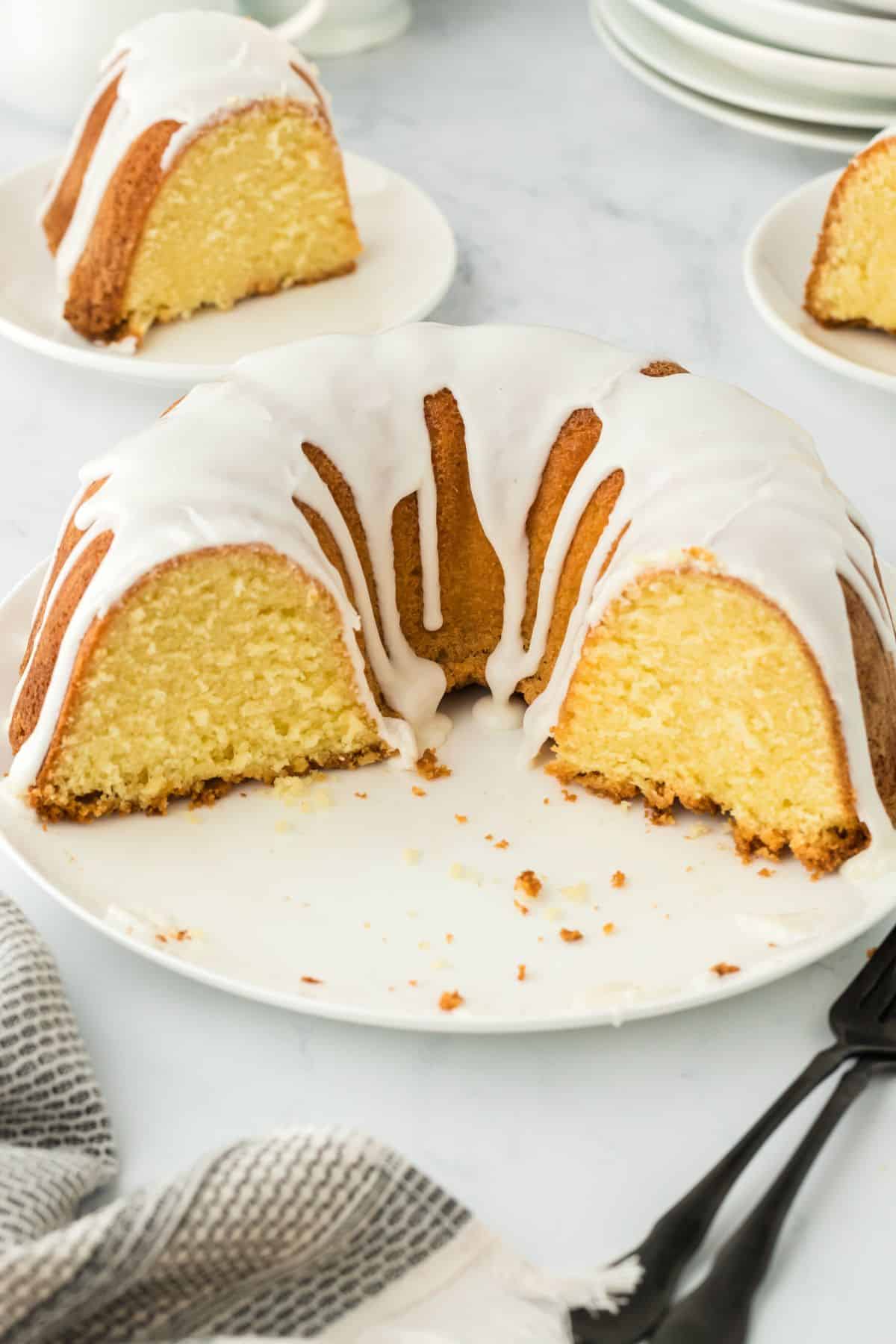 Five flavor pound cake with a section removed, showing the soft, yellow interior, with crumbs scattered on the plate and more cake slices in the background