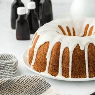 Five flavor pound cake with white icing, surrounded by bottles of extracts and a folded cloth in the foreground