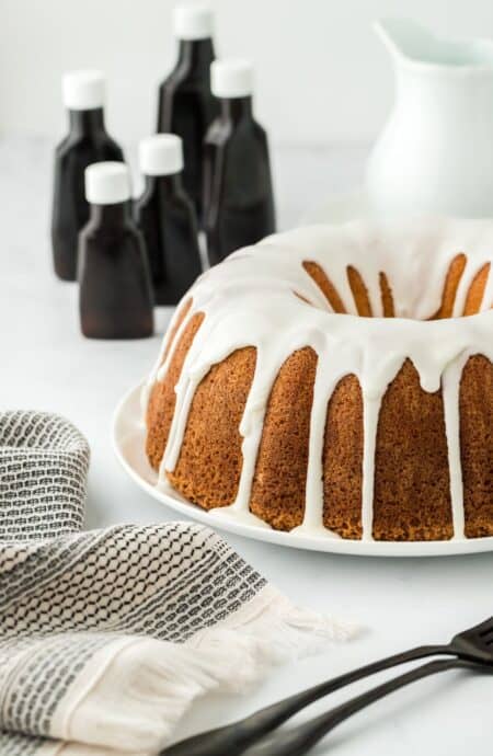 Five flavor pound cake with white icing, surrounded by bottles of extracts and a folded cloth in the foreground