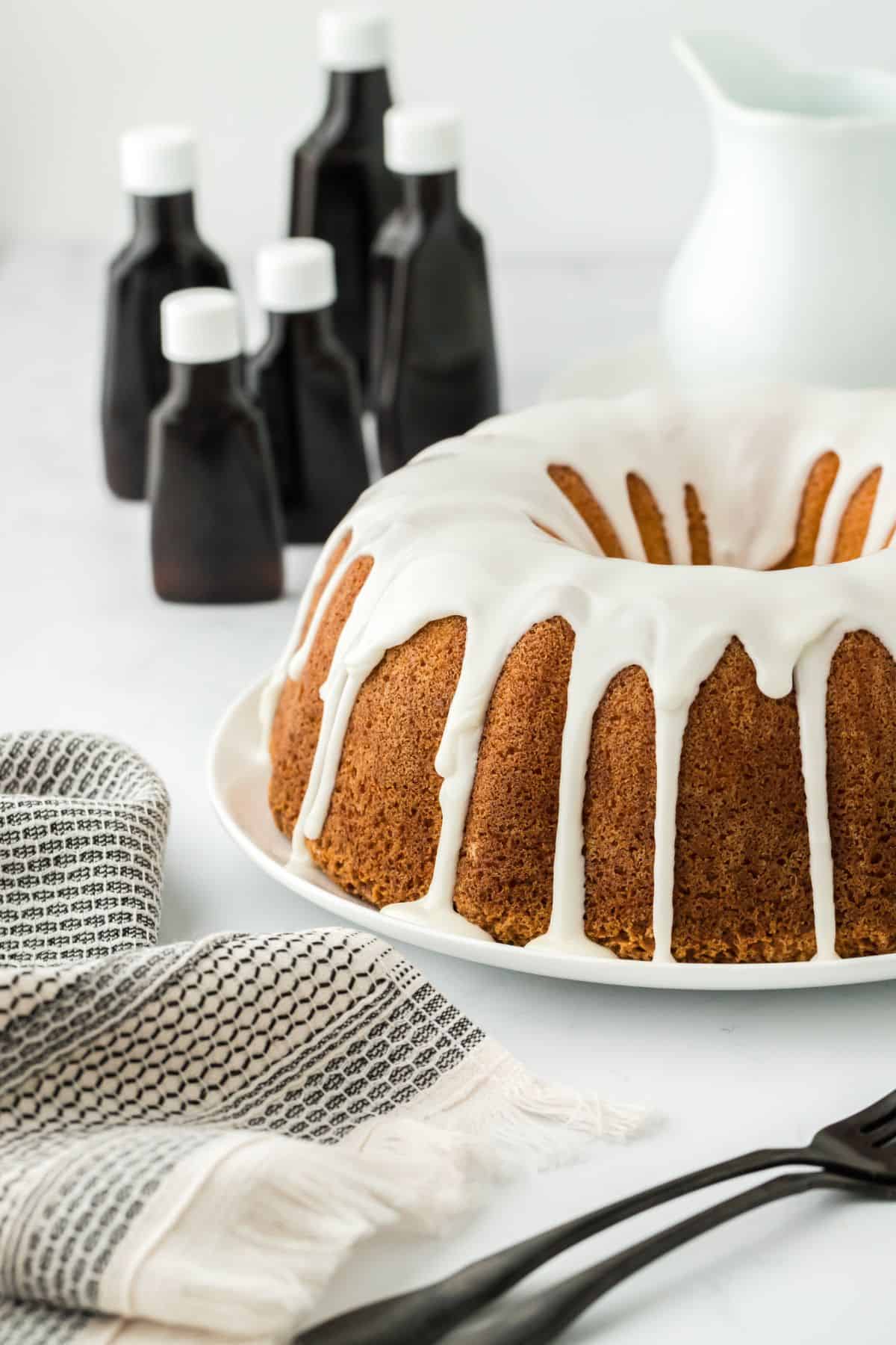 Five flavor pound cake with white icing, surrounded by bottles of extracts and a folded cloth in the foreground