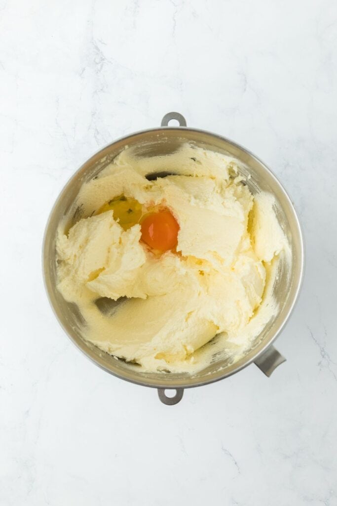 A mixing bowl showing creamed butter and sugar with an egg added