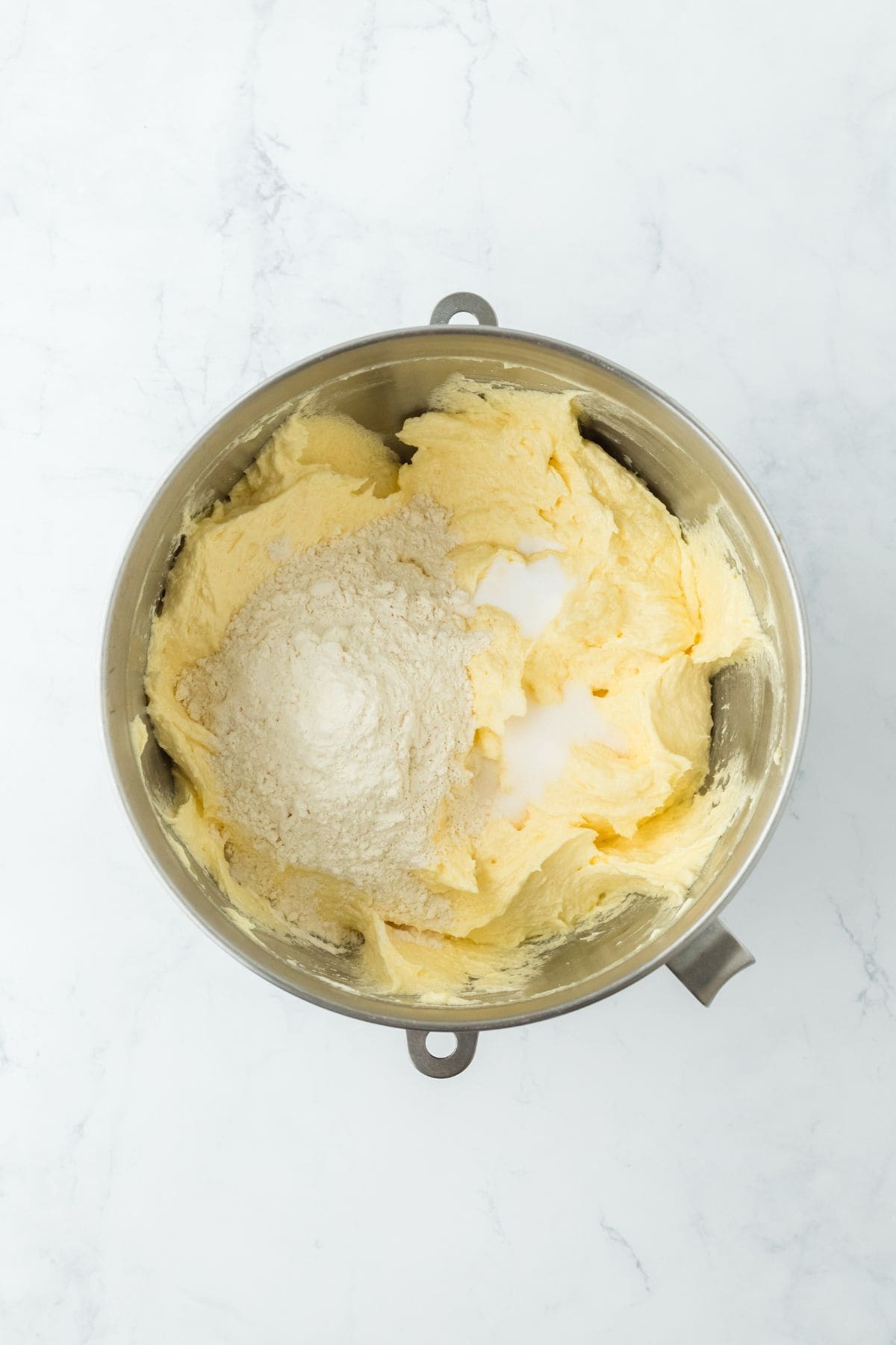 A mixing bowl containing creamed ingredients with flour added on top