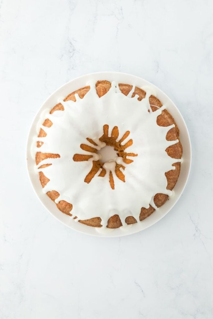 An overhead view of a five flavor pound cake with white icing drizzled over it, fully coated on a white plate