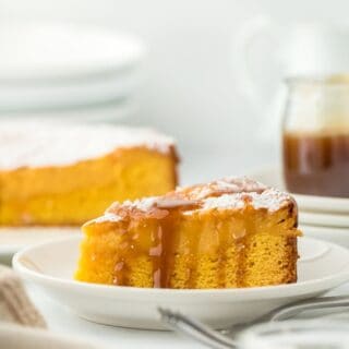 A gooey brown butter cake slice with a drizzle of caramel sauce, showcasing the rich, golden interior with the rest of the cake and a caramel jar in the background