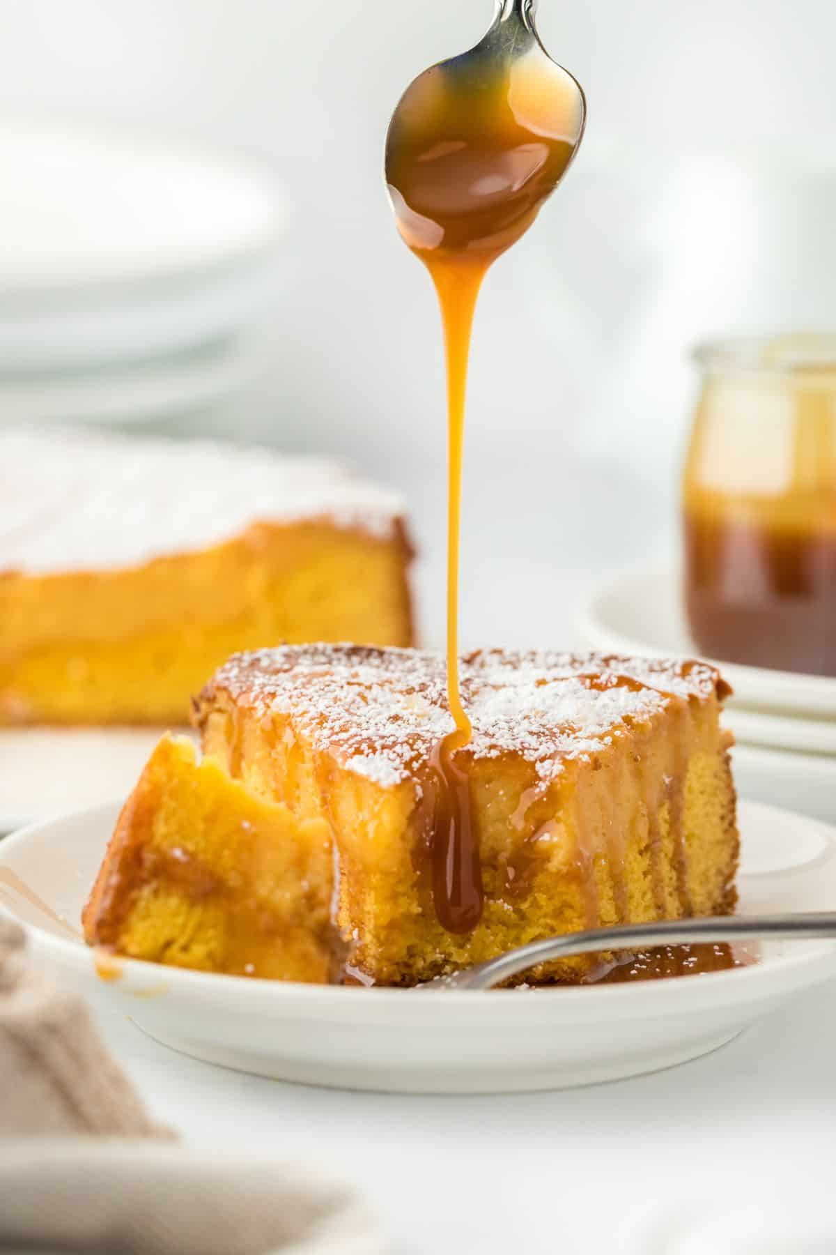 A fork lifting a piece of gooey brown butter cake, with caramel sauce being drizzled over the top with a spoon