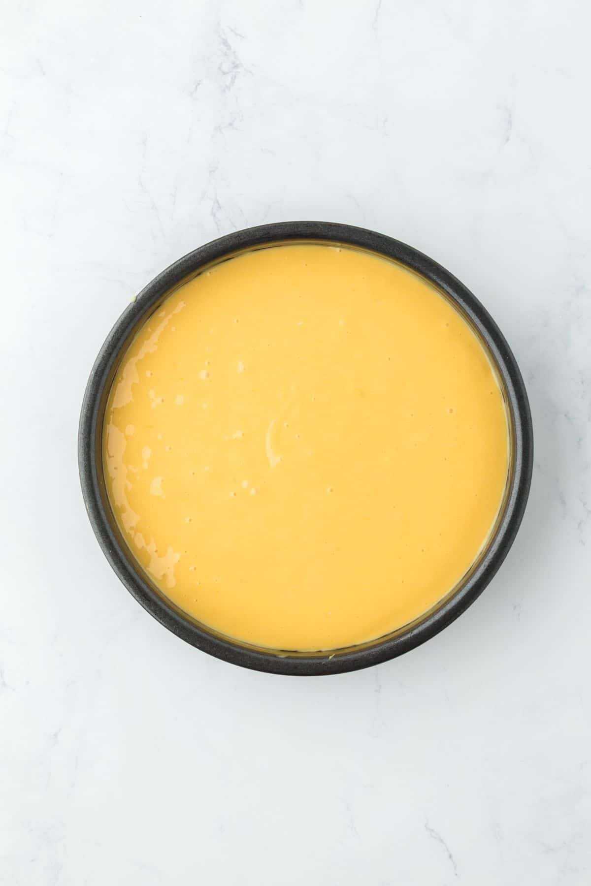 Cream cheese mixture spread on top of the cake batter in a round baking pan, ready for the oven