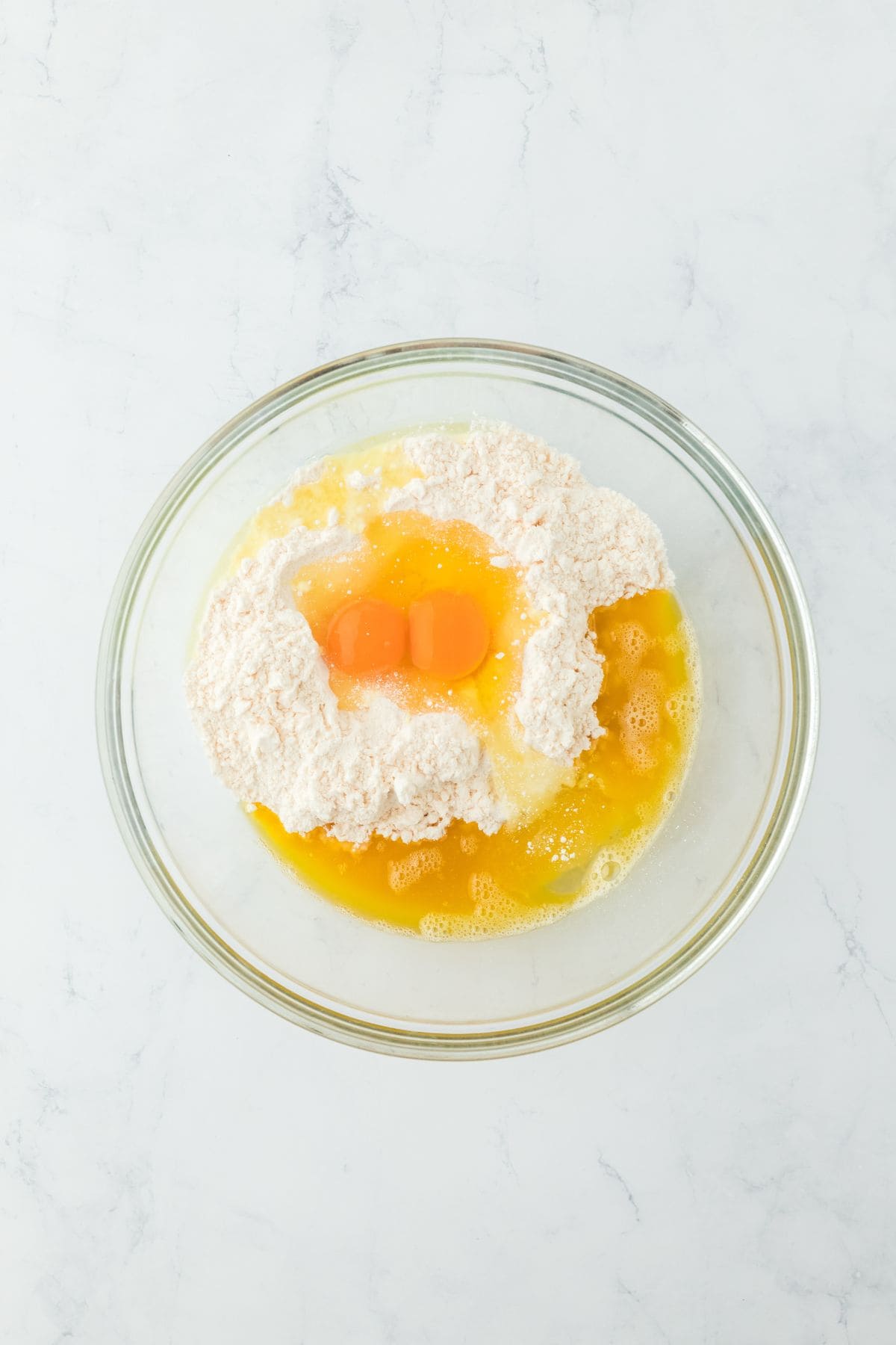 Two raw eggs with flour and other ingredients in a glass mixing bowl, ready to be mixed