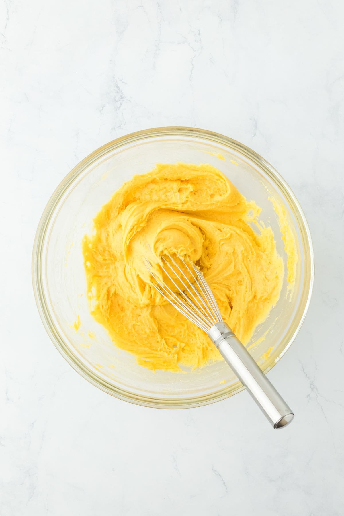 Smooth yellow batter in a glass bowl, mixed with a whisk