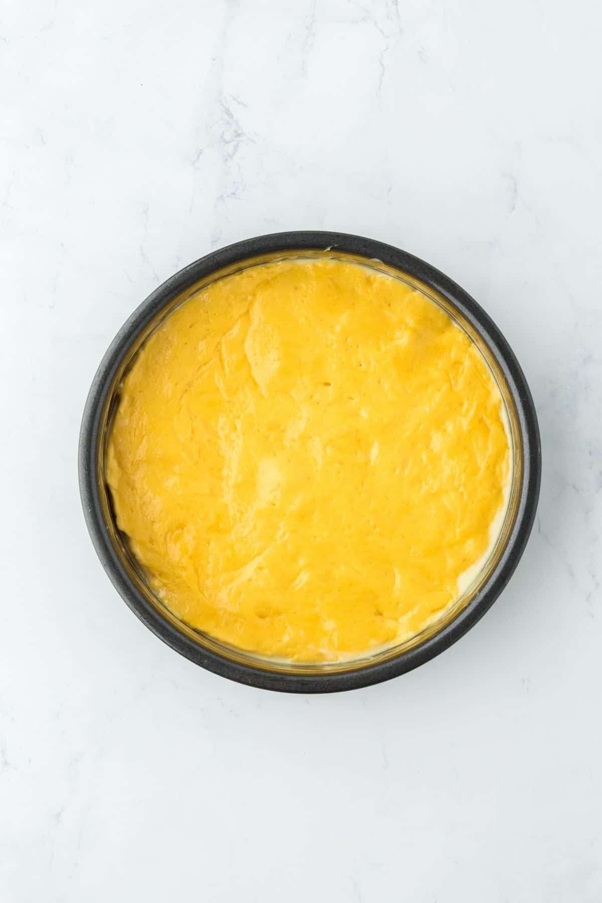 Yellow cake batter spread evenly in a round baking pan, ready for baking