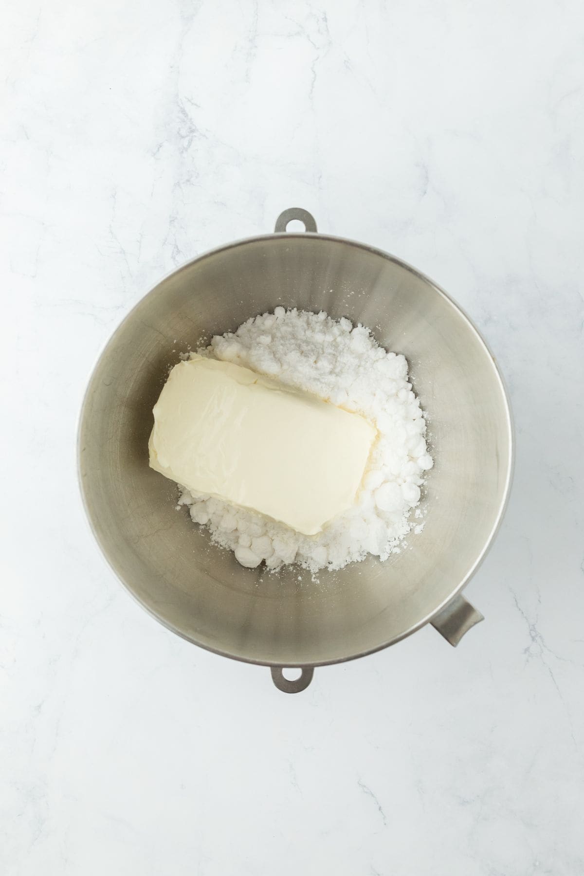 Cream cheese and powdered sugar in a metal mixing bowl, prepped for mixing