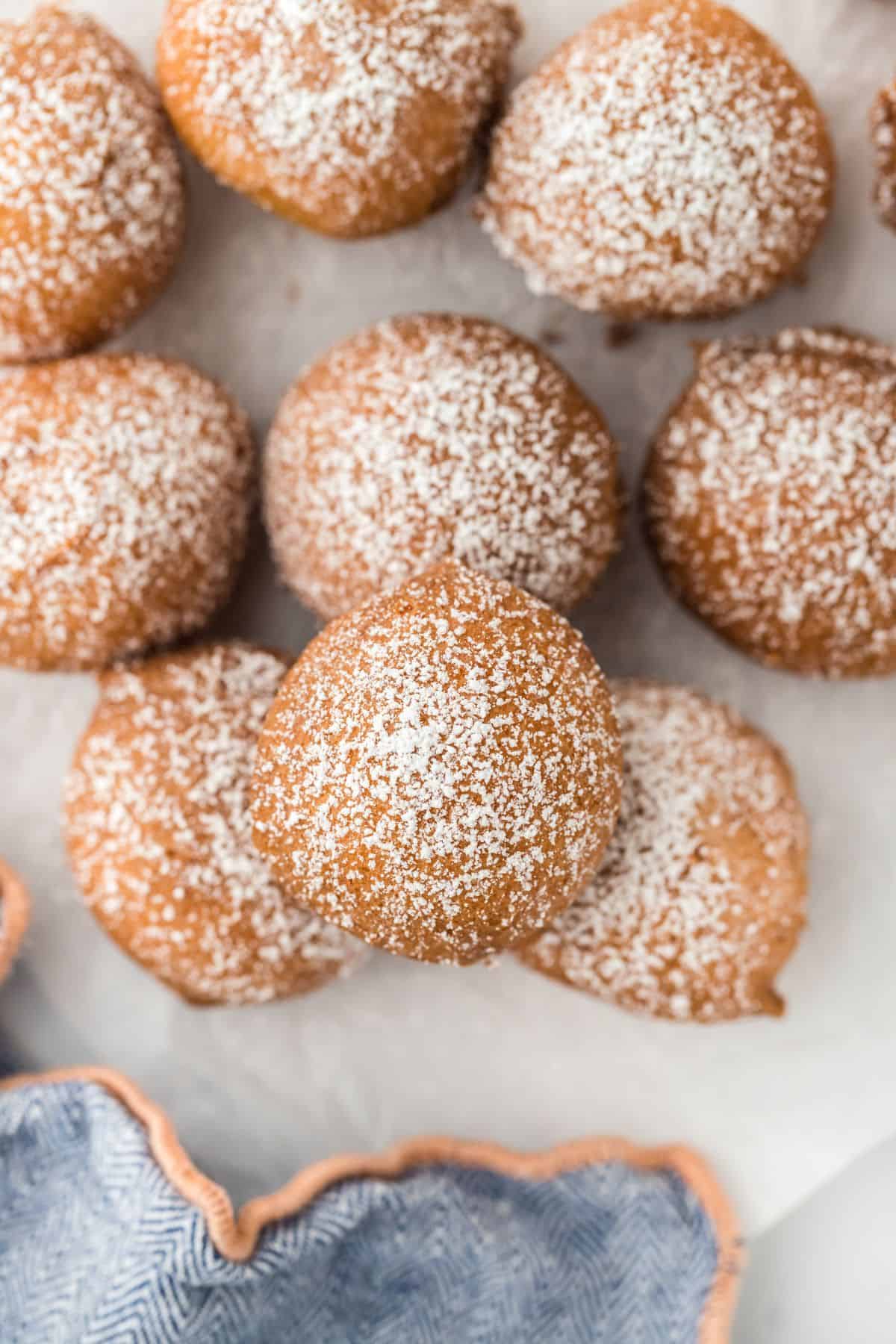 Closeup of multiple round, golden-brown pound cake beignets dusted with powdered sugar