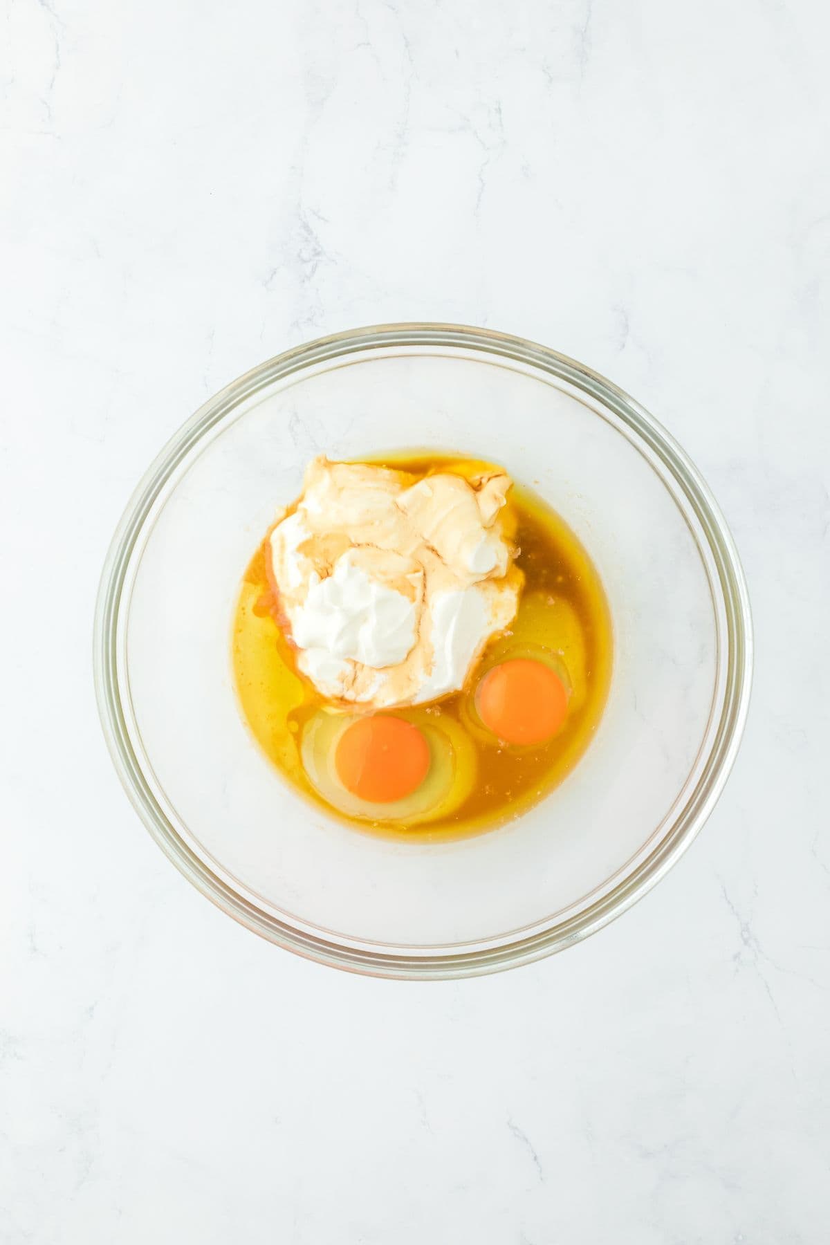 A glass bowl containing eggs, sour cream, vanilla and melted butter, ready to be mixed