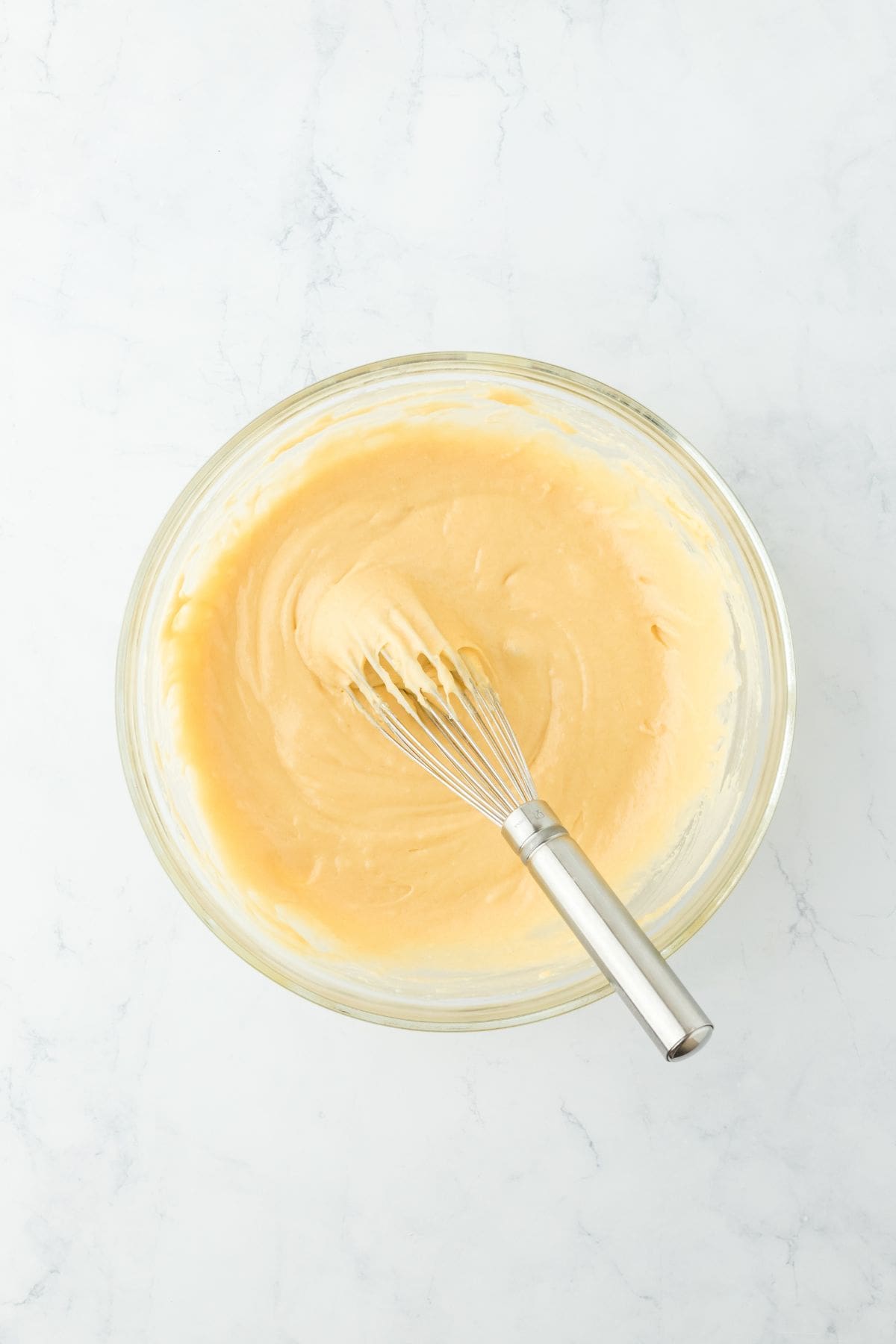 A smooth batter mixture in a glass bowl with a whisk resting inside