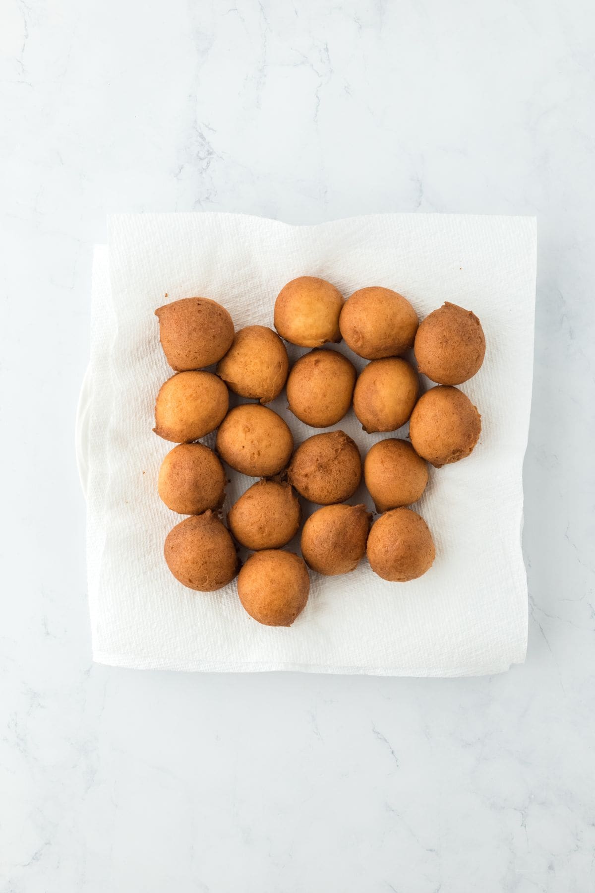 A collection of golden-brown fried beignets placed on a white paper towel to drain excess oil