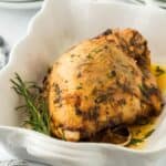 A golden-brown roasted turkey breast seasoned with herbs, garnished with lemon slices and fresh rosemary in a white baking dish