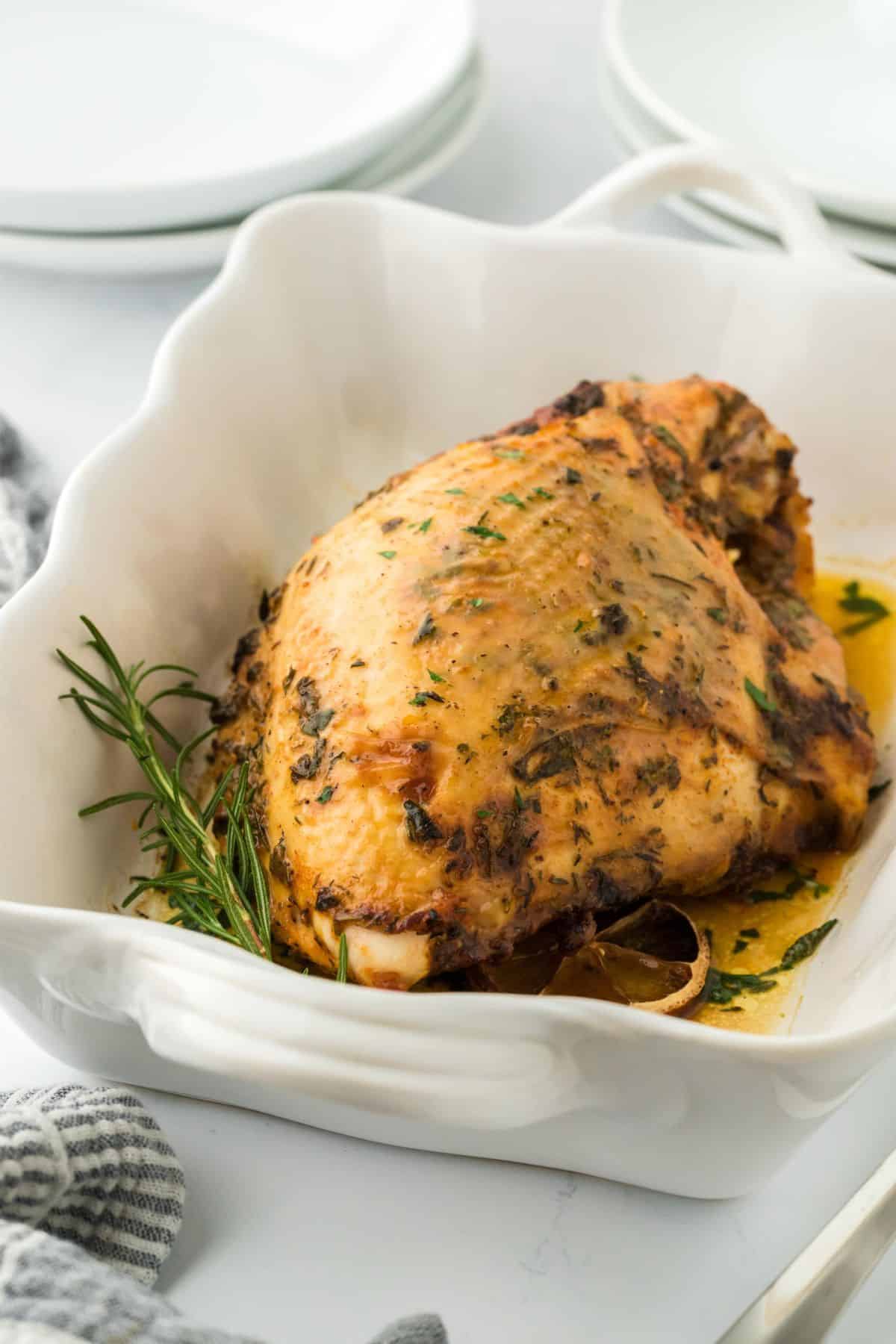 A golden-brown roasted turkey breast seasoned with herbs, garnished with lemon slices and fresh rosemary in a white baking dish