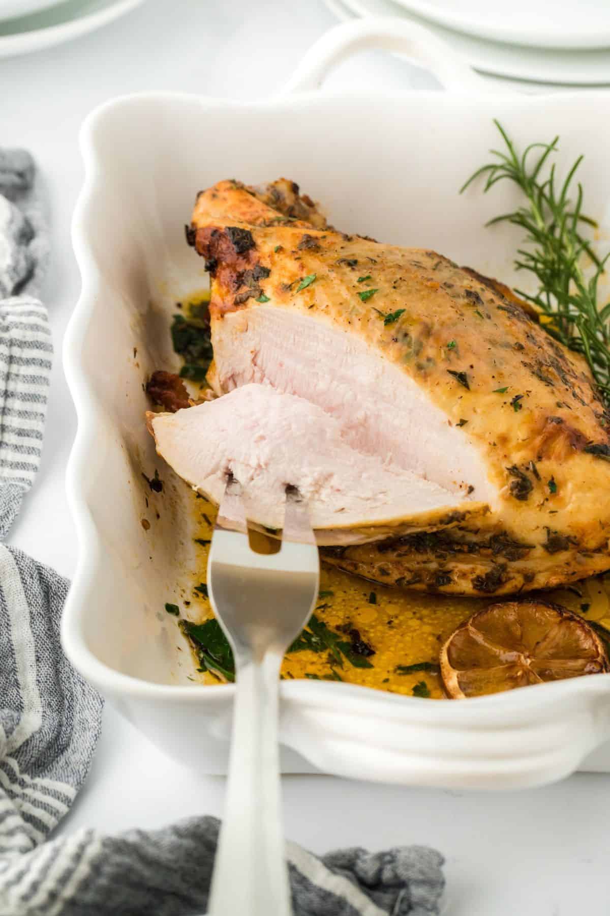 A partially sliced roasted turkey breast with a fork inserted, showing the juicy, tender white meat