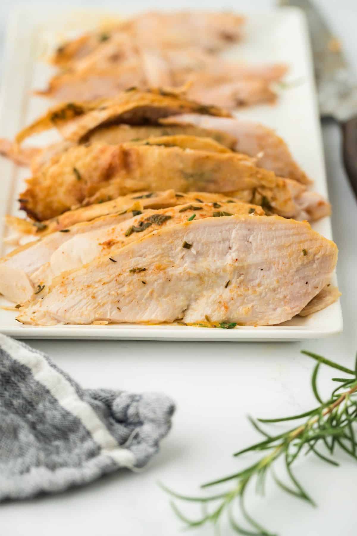 A white platter with neatly sliced roasted turkey breast, seasoned and garnished with herbs