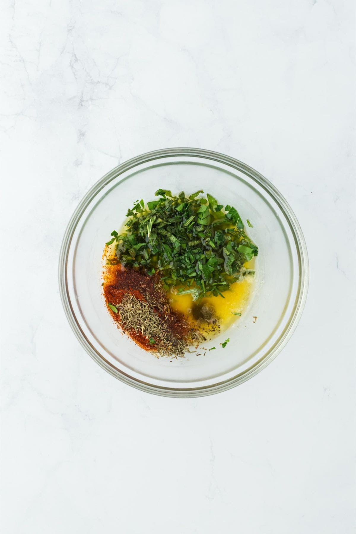 A clear bowl filled with fresh chopped herbs, spices, and melted butter for seasoning