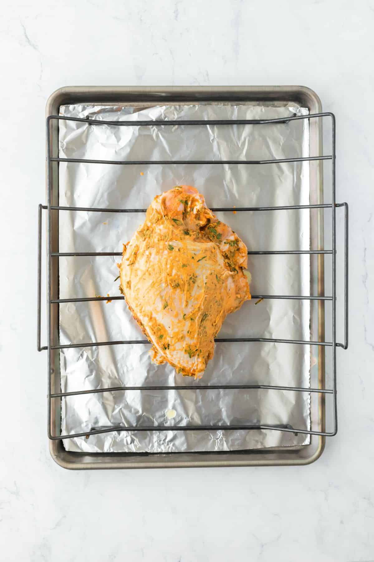 A seasoned turkey breast resting on a baking rack lined with foil, ready for roasting