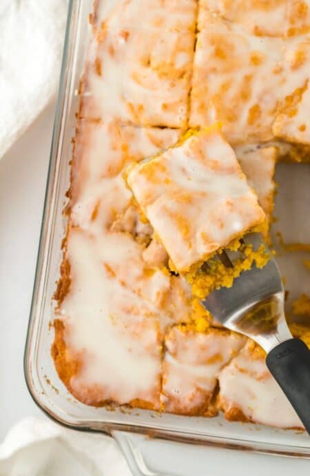 Sweet Potato Honey Bun Cake in a glass baking dish, sliced into squares with one piece being served on a spatula