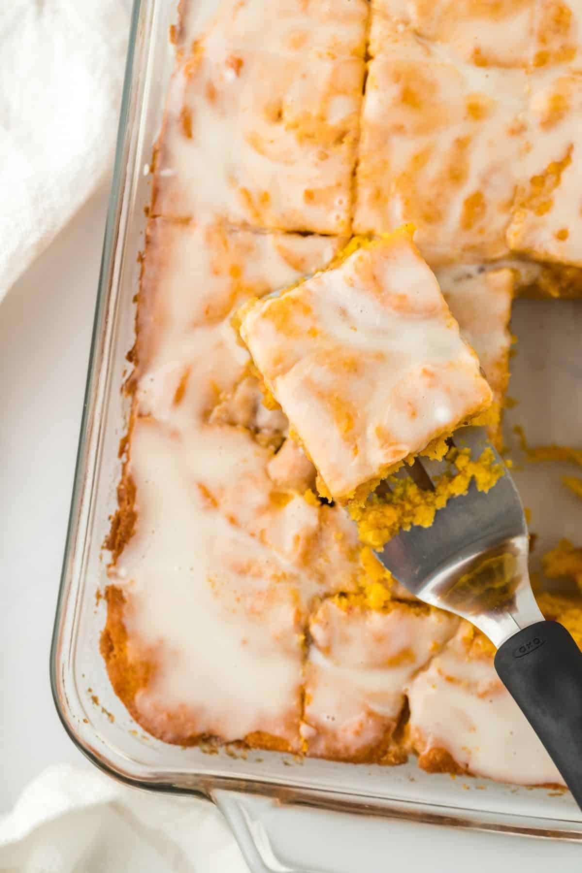 Sweet Potato Honey Bun Cake in a glass baking dish, sliced into squares with one piece being served on a spatula