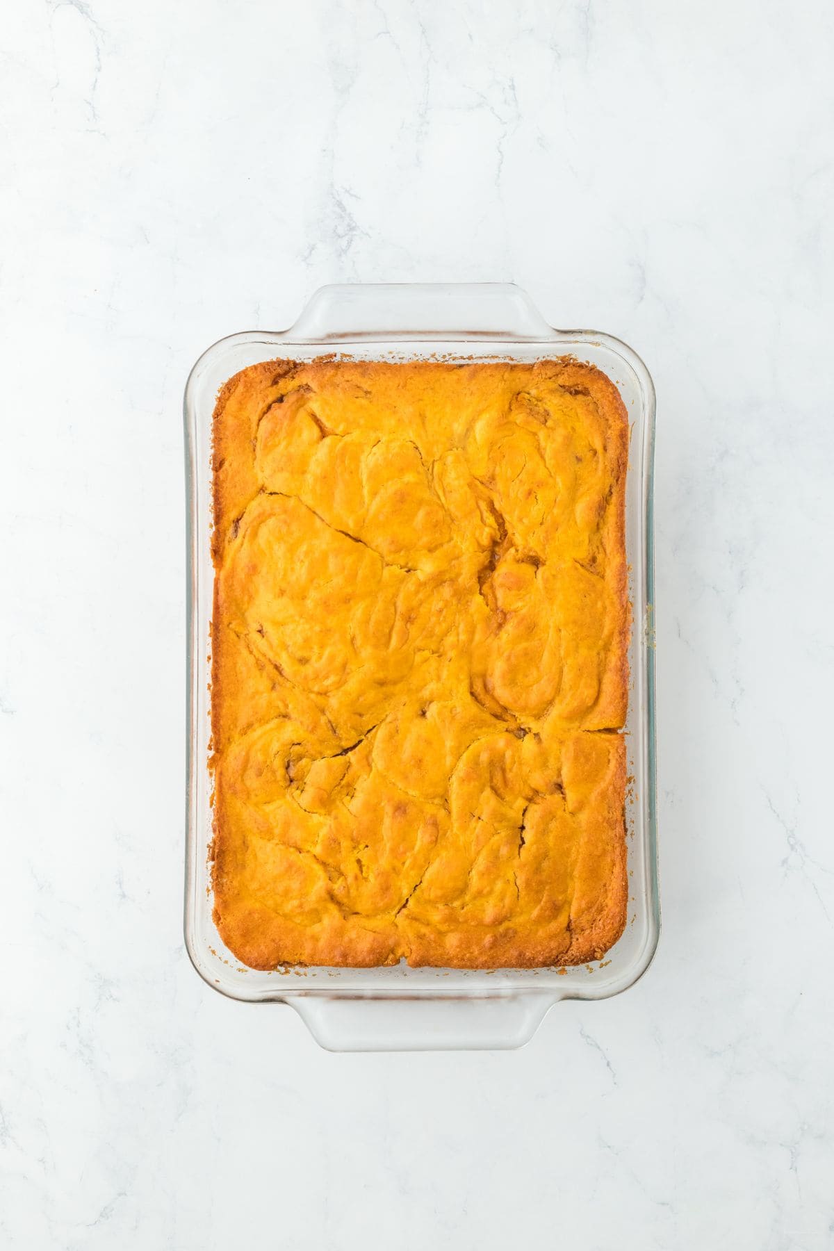 The baked cake in a glass dish, golden brown with visible swirls