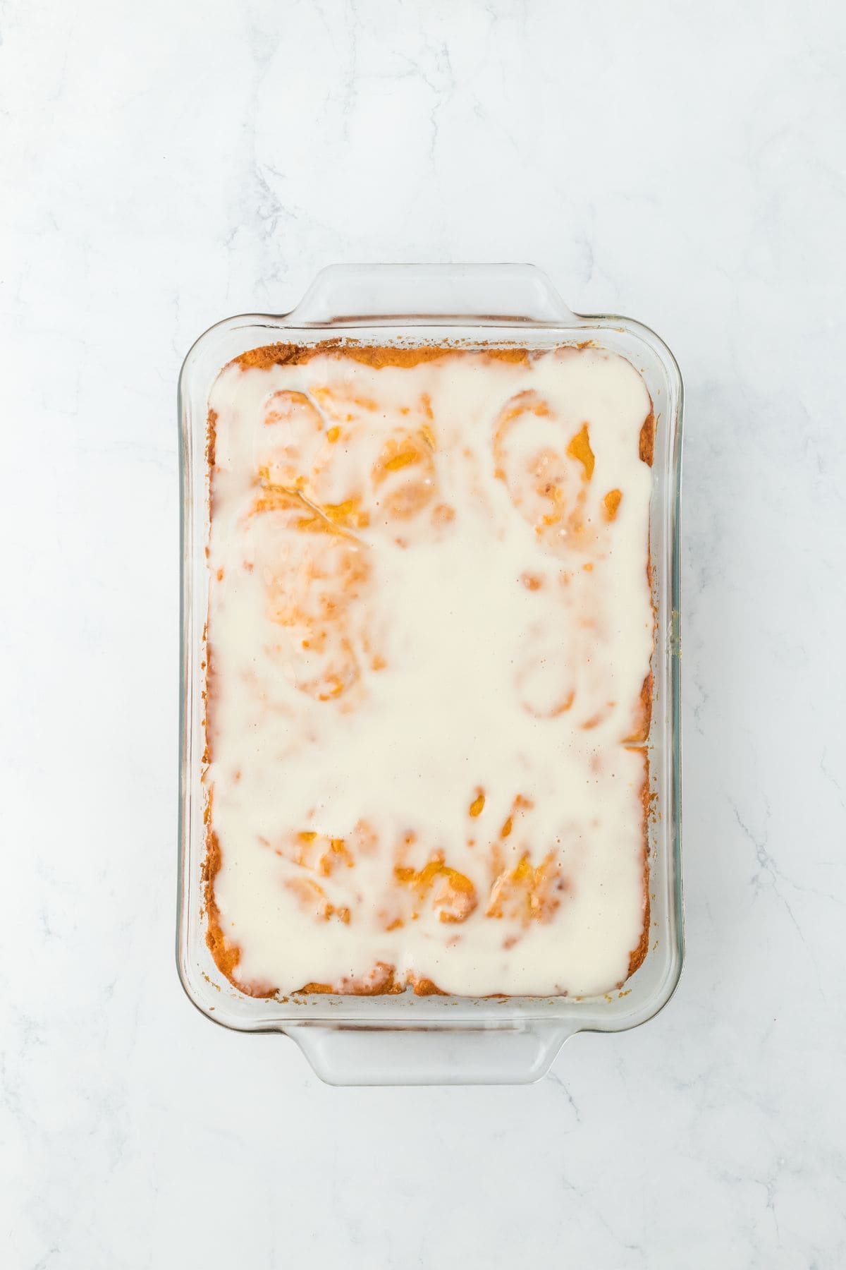 Sweet potato honey bun cake after glazing, with a shiny white icing coating the top in the baking dish