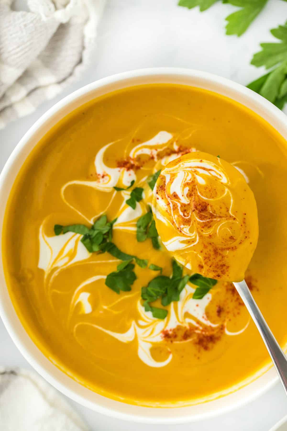 A spoonful of creamy sweet potato soup being lifted from the bowl, showing the smooth texture with swirls of cream and garnishes of paprika and parsley