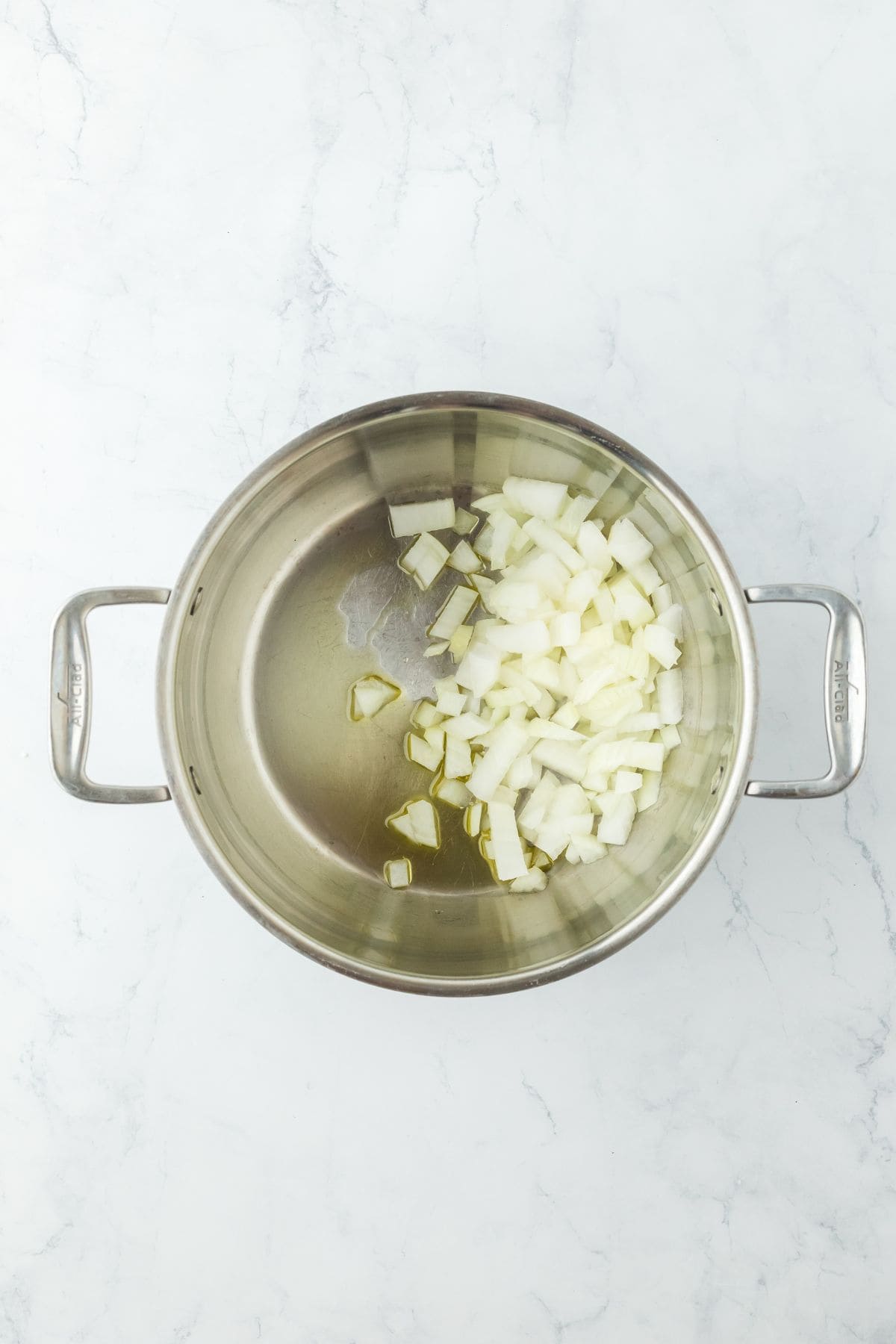 Overhead view of onions cooking in olive oil in a stainless steel pot