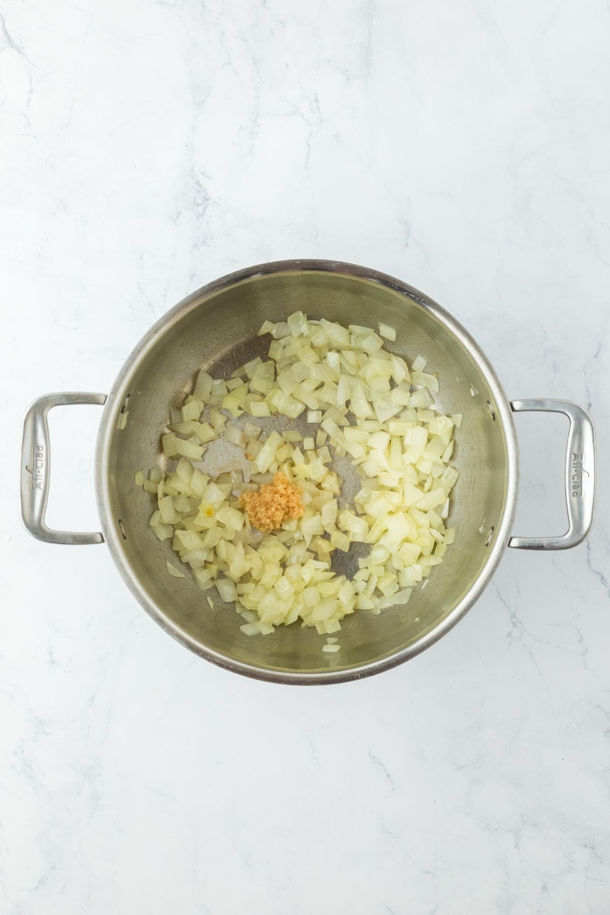 Onions cooking with a spoonful of minced garlic added in a stainless steel pot