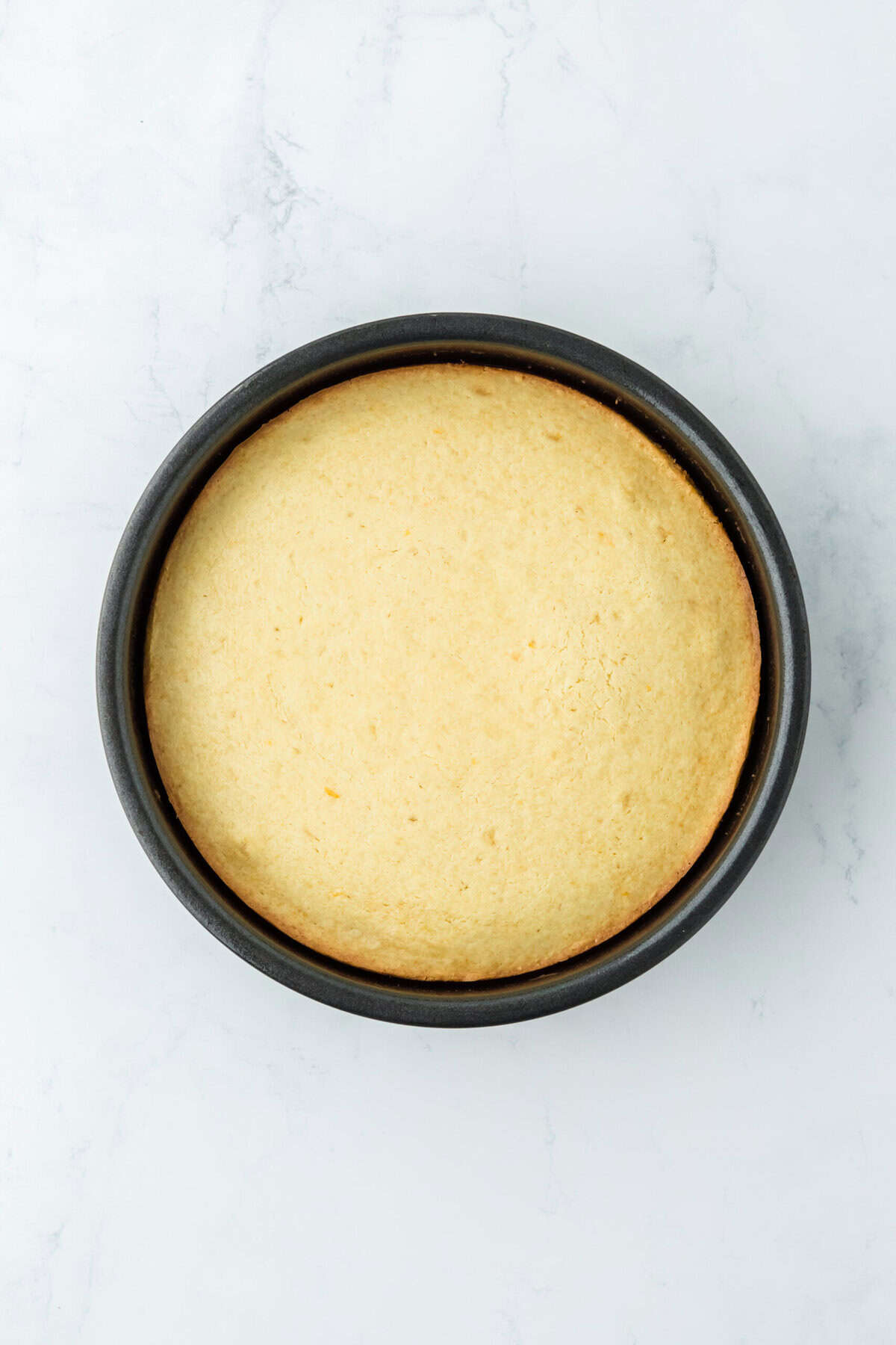 Baked orange cake in a round pan on white countertop