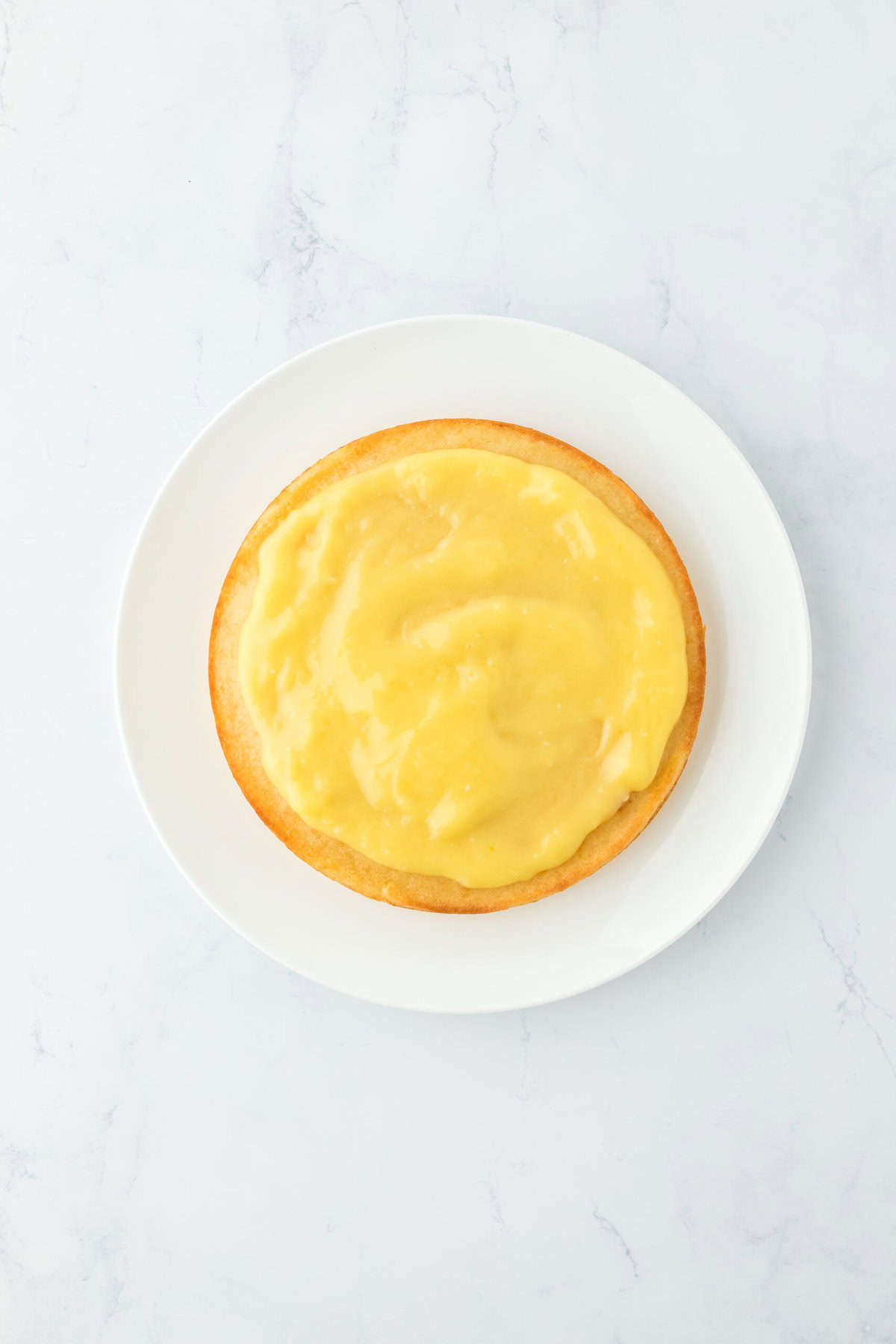 Orange curd spread on a layer of orange coconut cake on white countertop