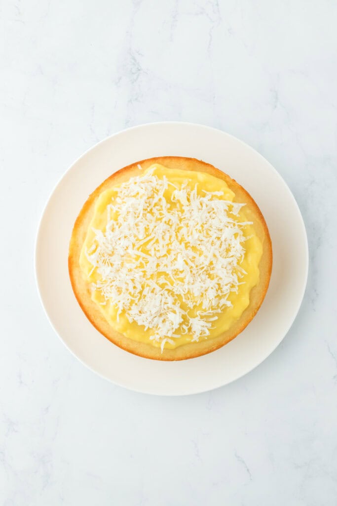 A layer of coconut cake with orange curd and coconut flakes on top
