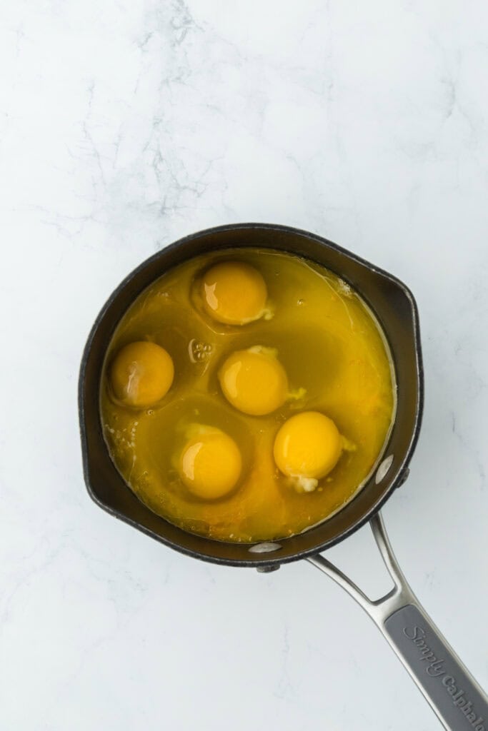 Eggs, orange juice, sugar, zest and orange juice in a saucepan on white countertop